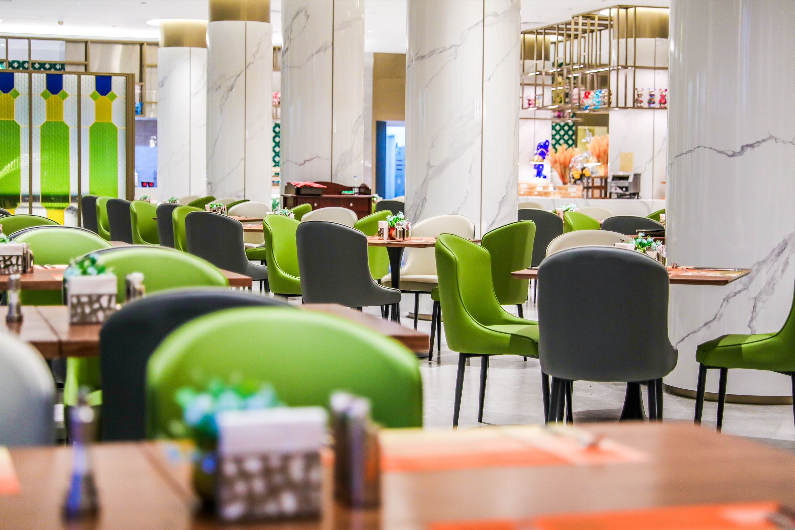 Ein modernes Restaurant mit grün-grauen Stühlen, Marmorkolonnen und einem klaren, zeitgemäßen Design.