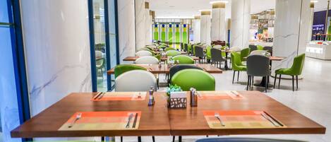 A modern restaurant with marble columns, green and grey chairs, and neatly arranged tables with cutlery.