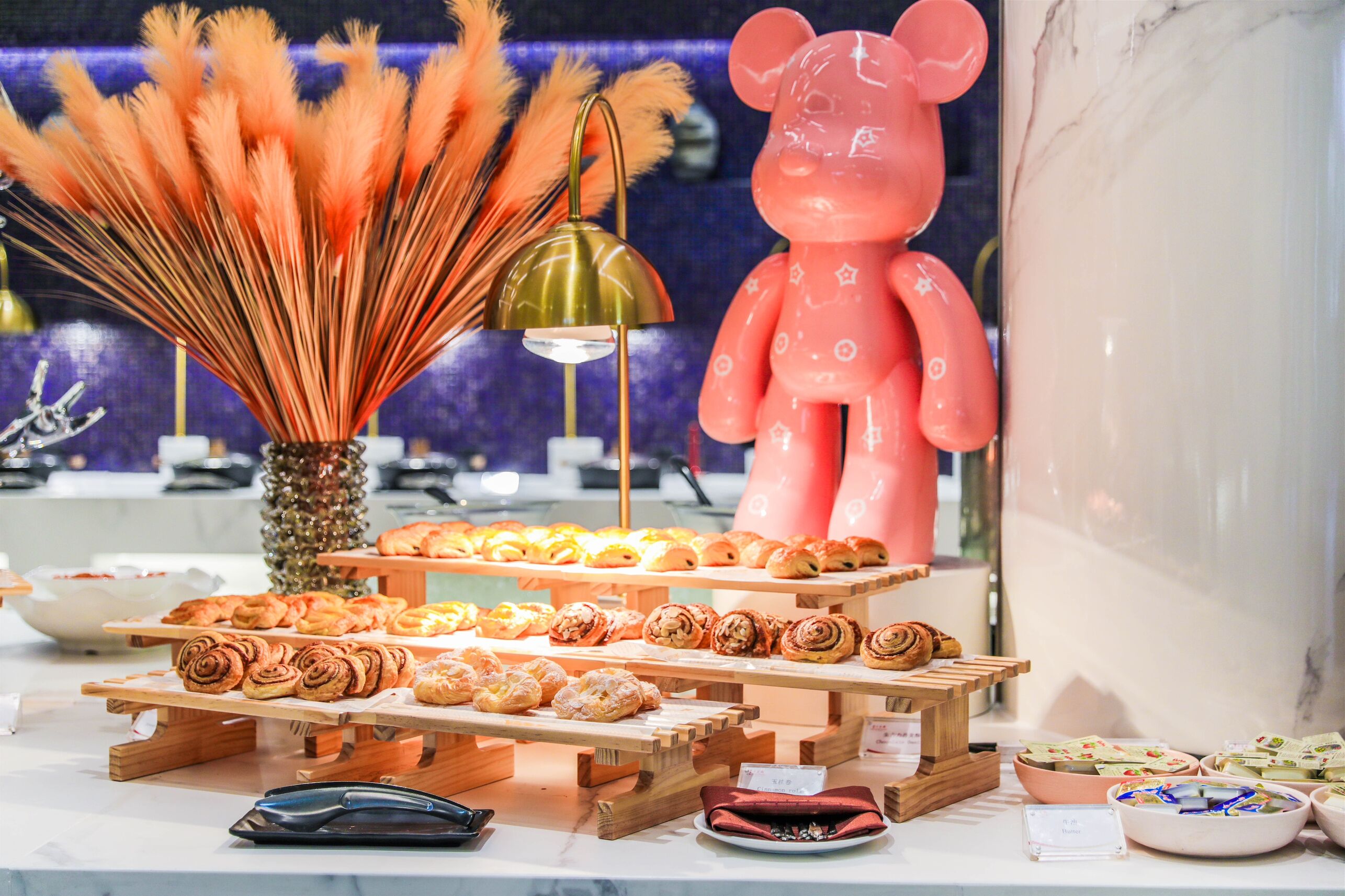 A display of pastries on wooden stands with a decorative bear figure and a vase of orange feathers.