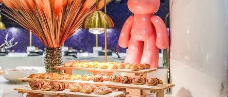 A display of pastries on wooden stands with a decorative bear figure and a vase of orange feathers.