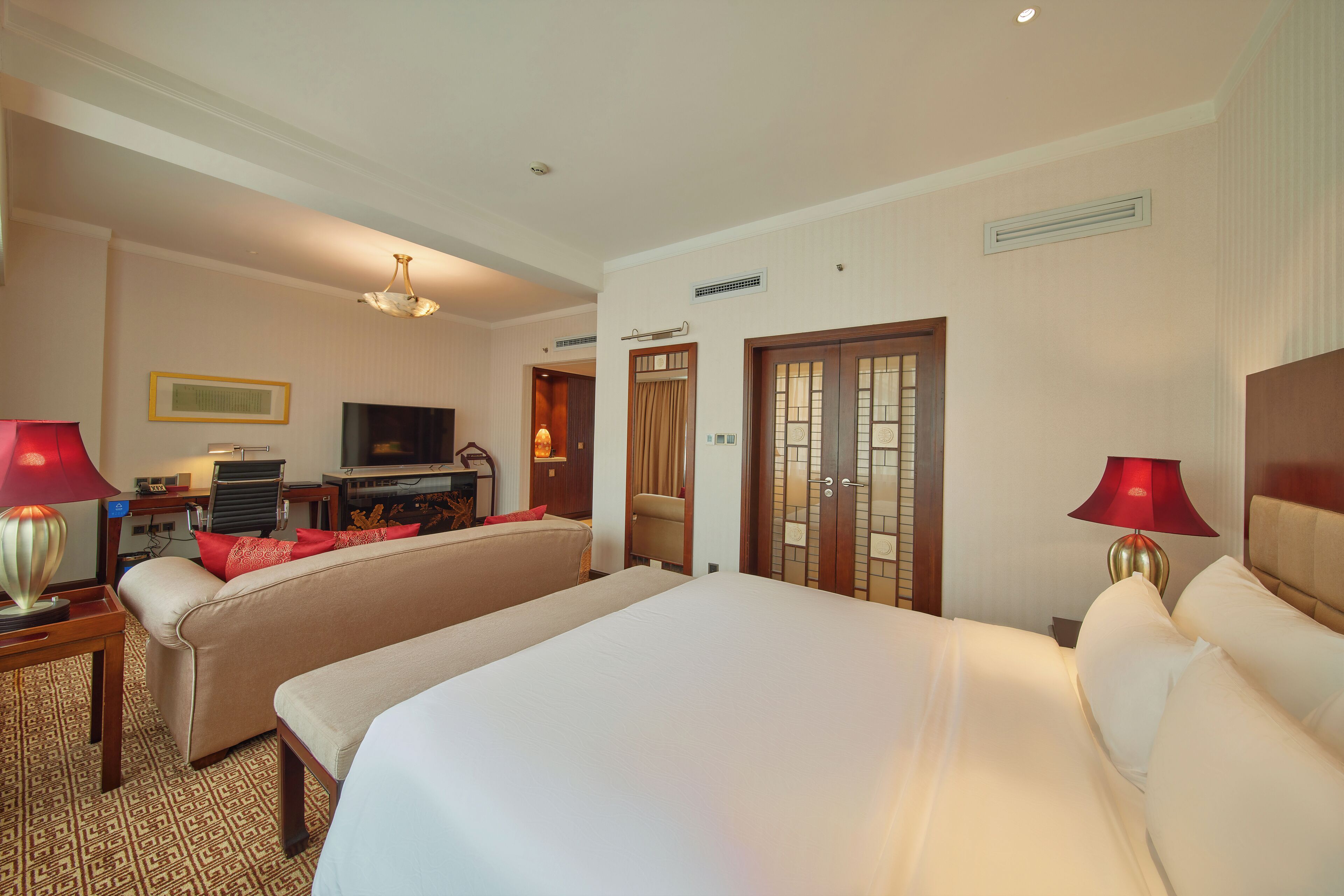 A hotel room with two beds, a desk, a television, and a red lamp.