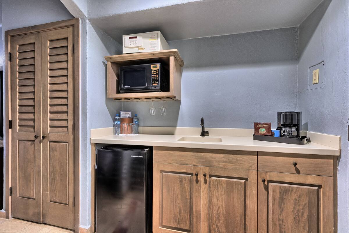 A compact kitchen with wooden cabinets, a built-in microwave, a refrigerator, and a coffee maker on the countertop.