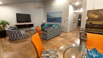 Ein modernes Wohnzimmer mit Flachbildfernseher, gemusterten Sofas, einem Glastisch und einem Essbereich mit Bar.