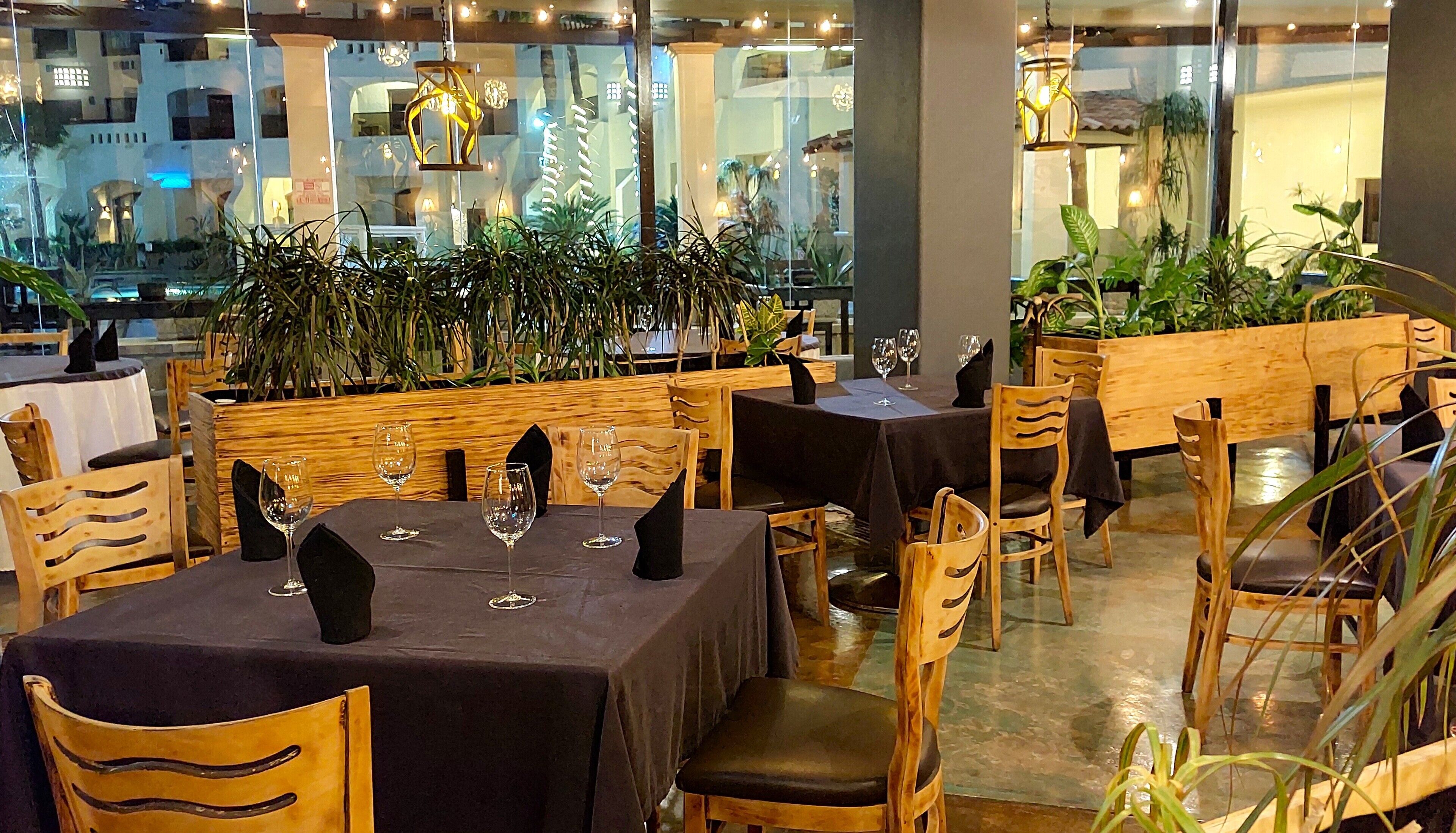 A restaurant with tables set for dining, wooden chairs, and potted plants.