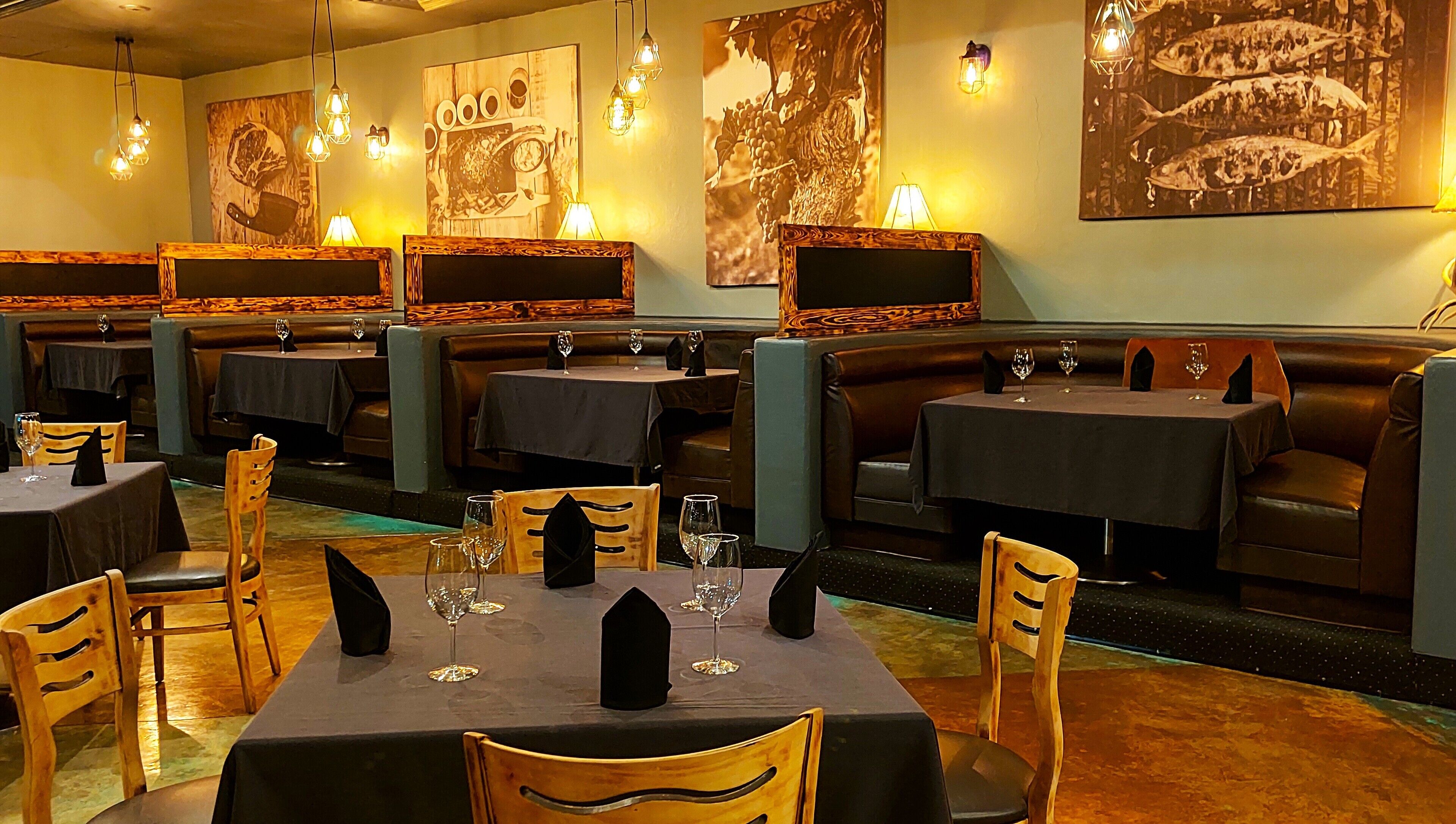 A restaurant with booths and tables, each with a wine glass and napkin.