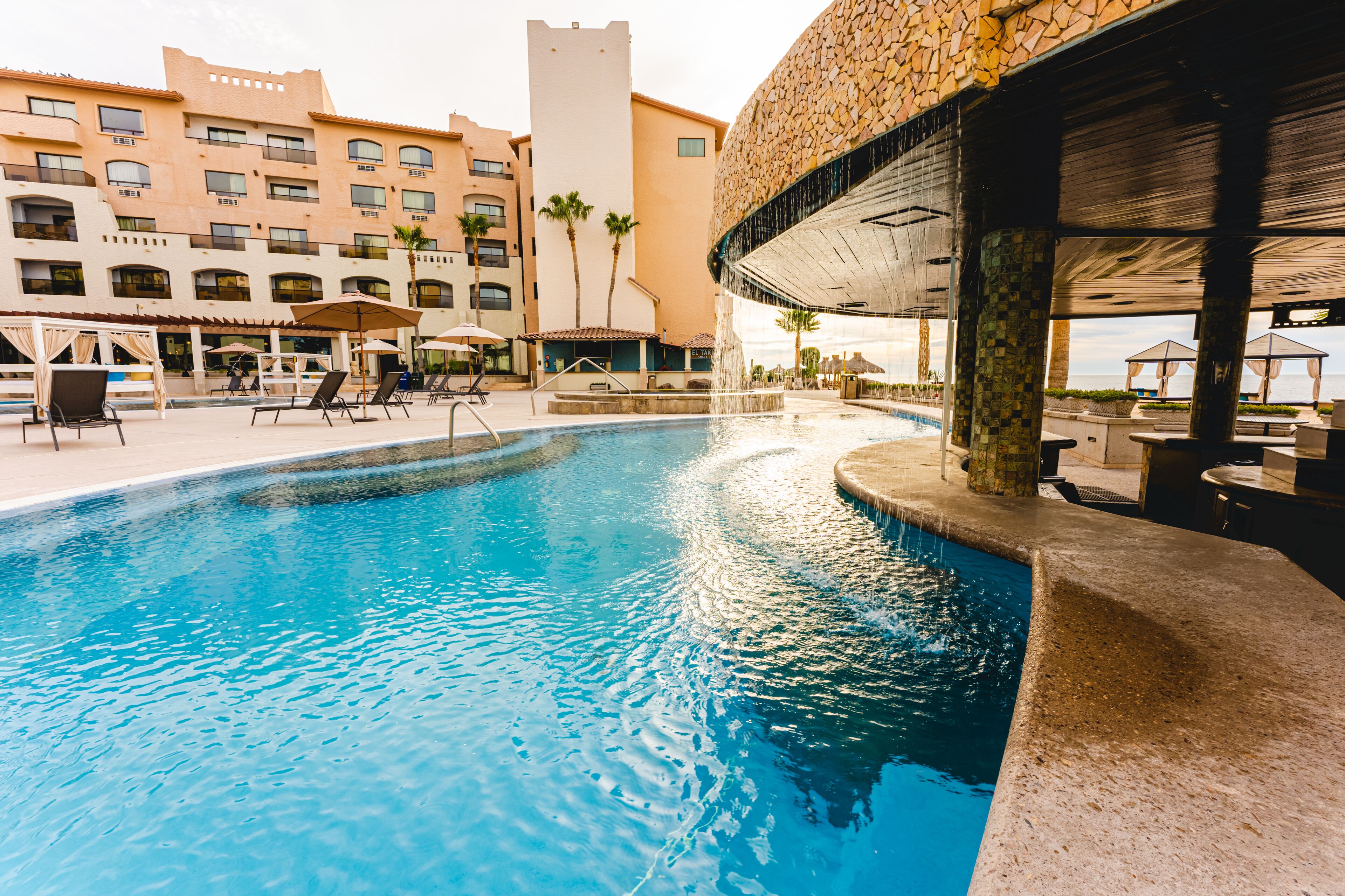 A swimming pool with lounge chairs and umbrellas, a stone facade building, and a clear sky.