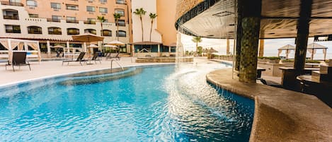 A swimming pool with lounge chairs and umbrellas, a stone facade building, and a clear sky.