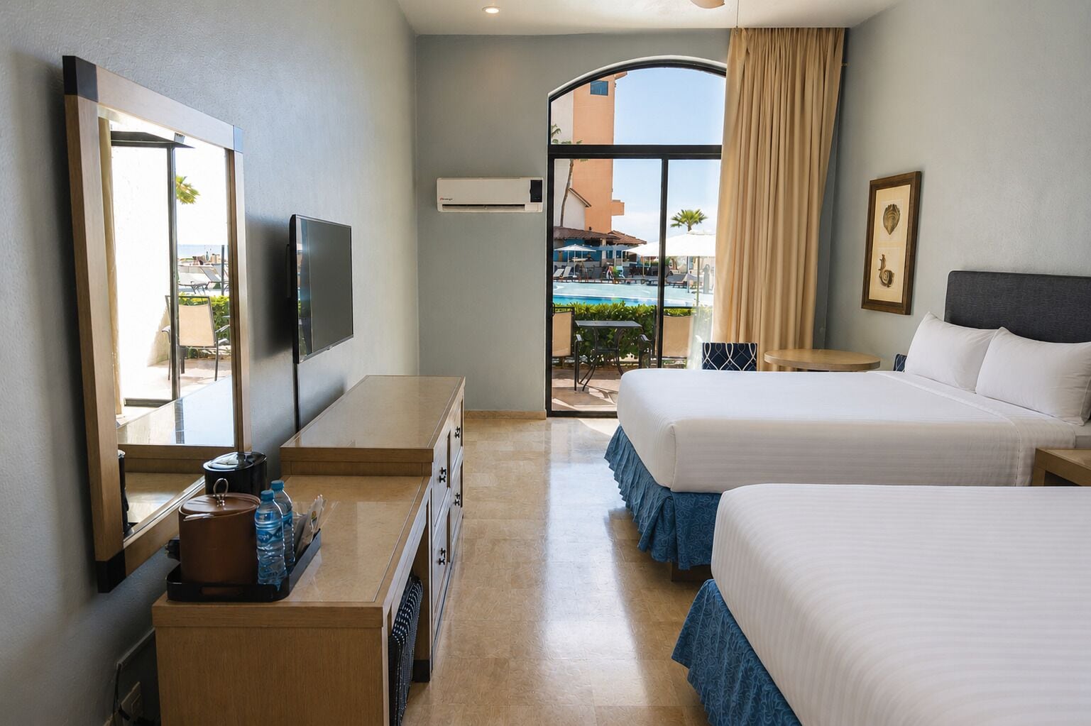 Camera d'albergo con letto, televisore, scrivania, comò e vista su un'area piscina.
