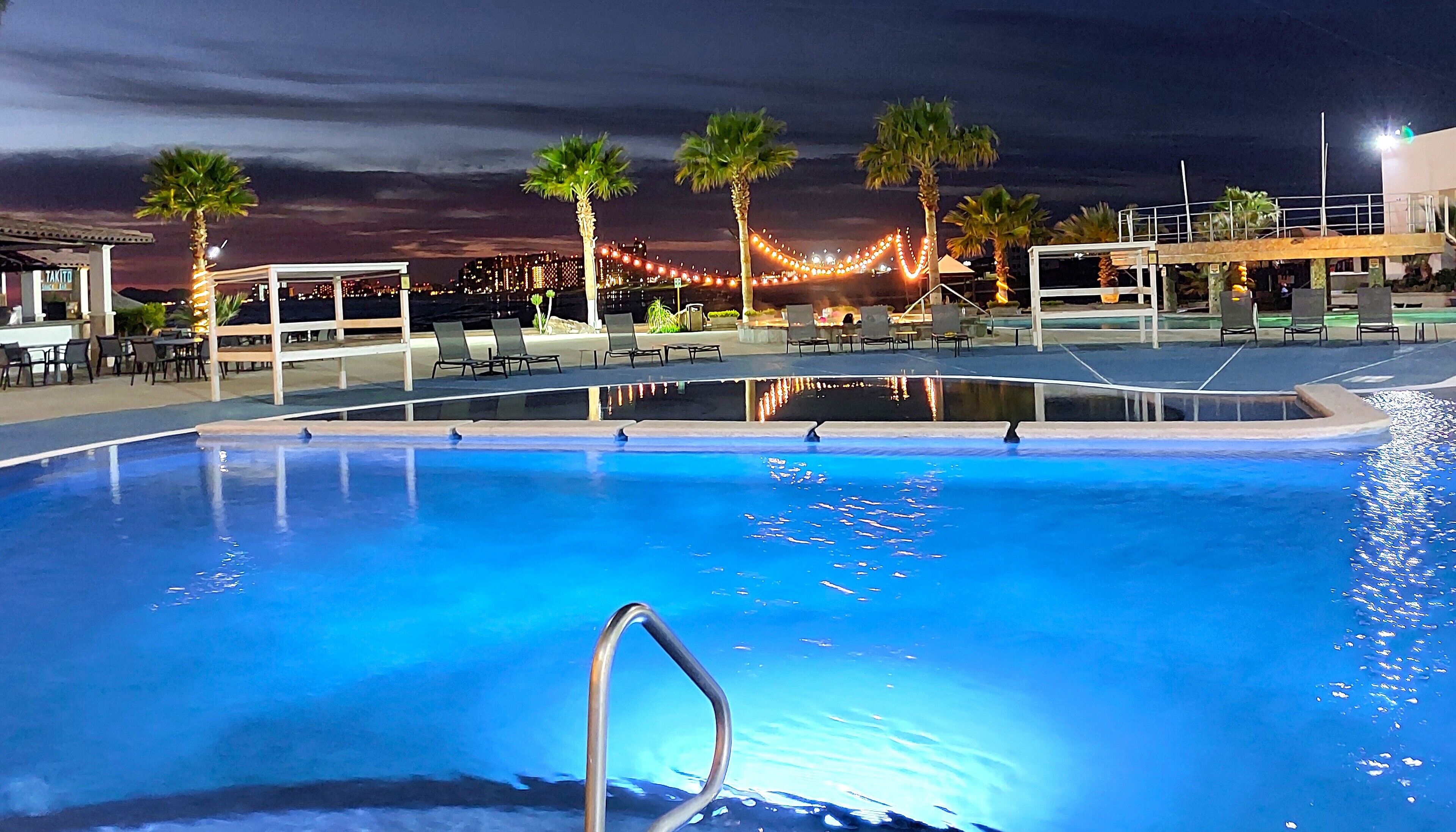 Ein Pool mit Metallleiter, umgeben von Palmen und Liegestühlen.