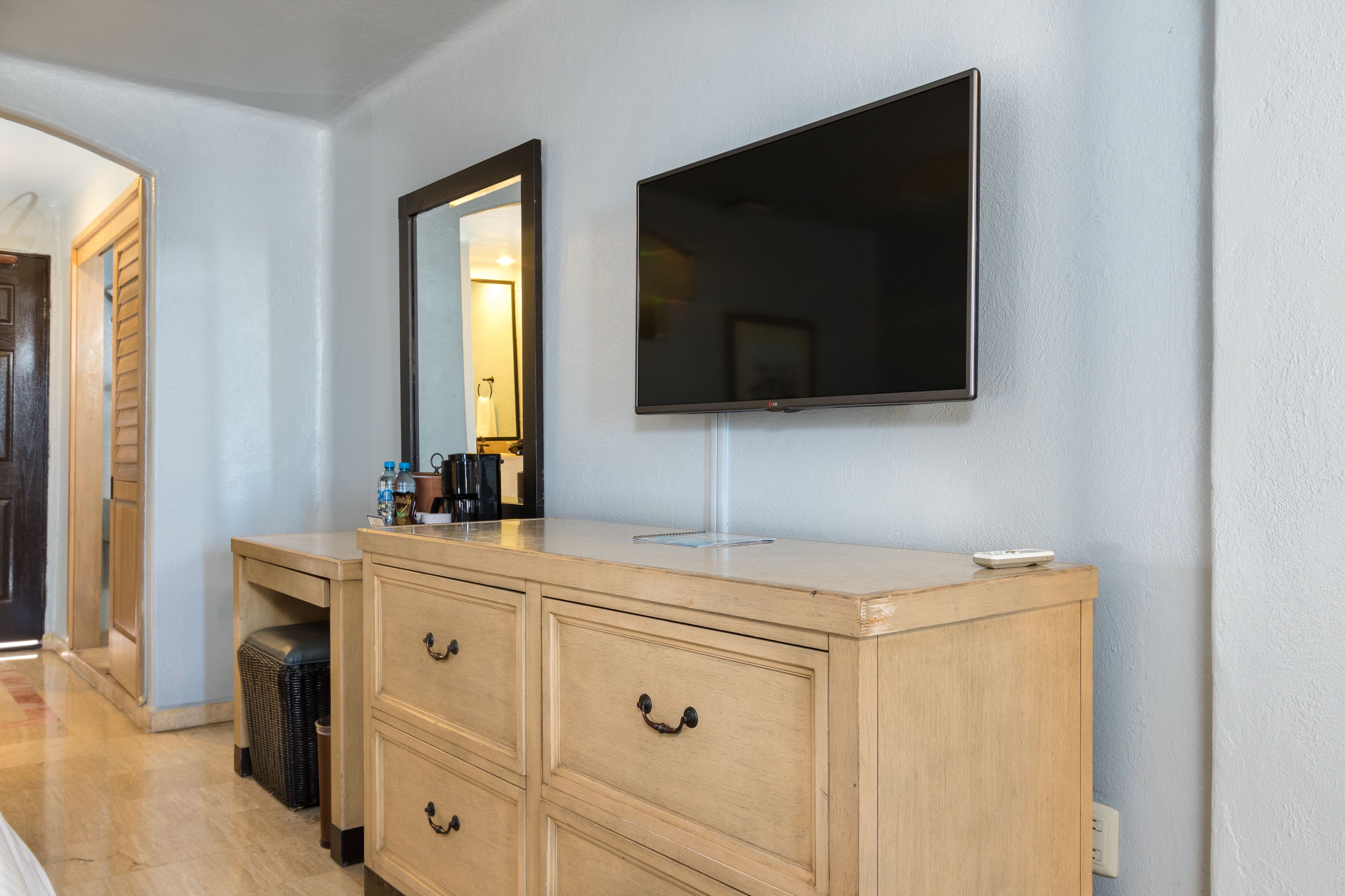 Habitación de hotel con tocador de madera, televisor de pantalla plana en la pared y espejo sobre el tocador.