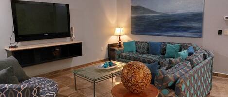Ein Wohnzimmer mit Flachbildfernseher, einem gemusterten Sofa, einem Couchtisch mit Dekoration und einem Bild an der Wand.