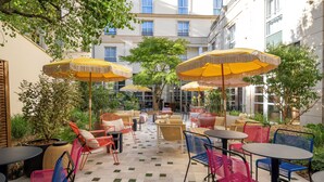 An outdoor café area with multiple tables and chairs, yellow umbrellas, and a tiled floor. - Urban Hive Paris (Paris)