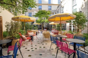 An outdoor café area with multiple tables and chairs, yellow umbrellas, and a tiled floor. - Urban Hive Paris (Paris)