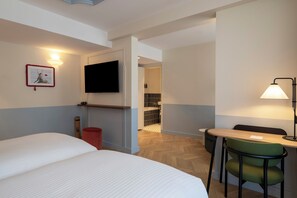 Une chambre d’hôtel avec un lit, un bureau et une chaise, une télévision et une salle de bain visible à travers une porte ouverte.