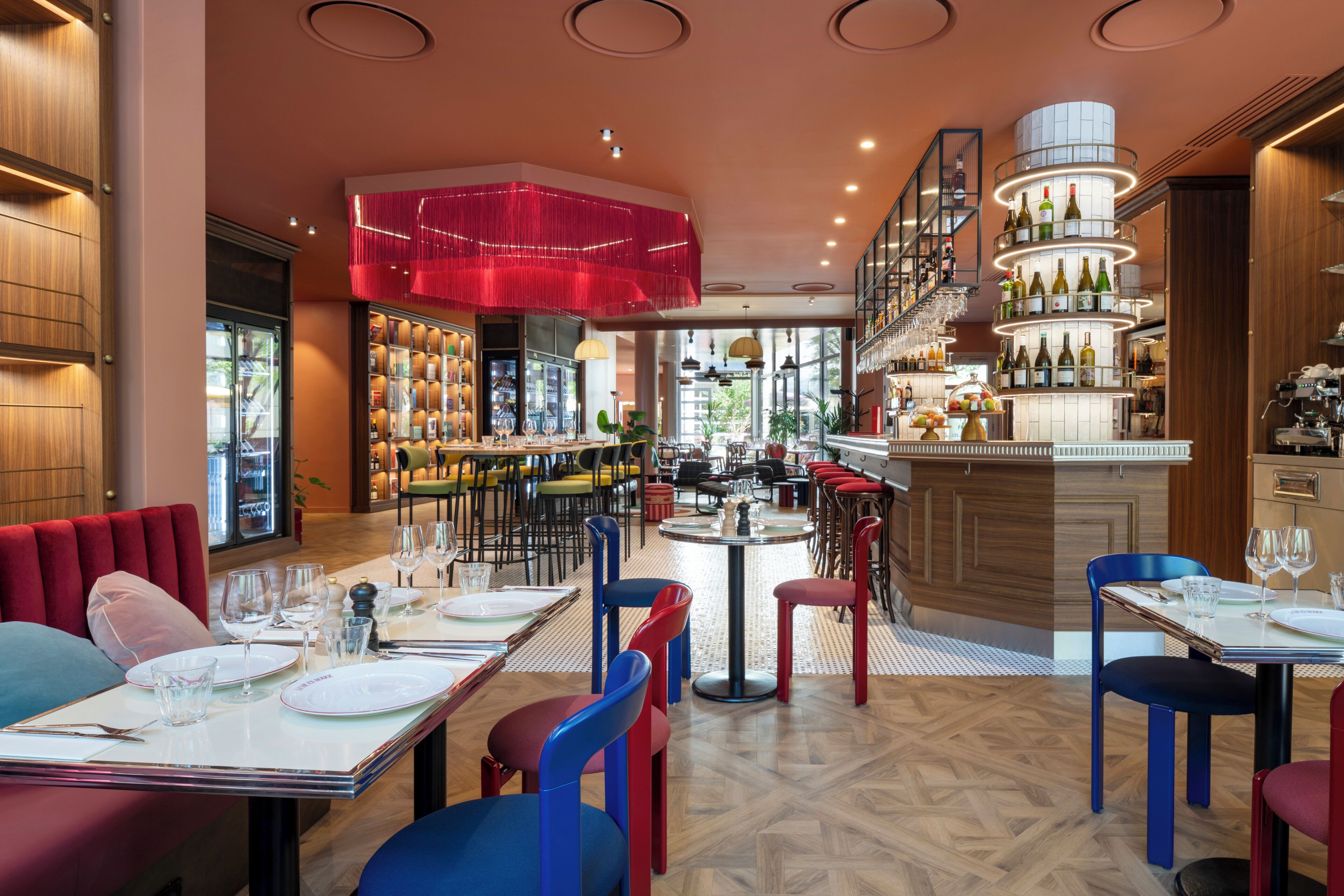 Un interior de restaurante con varias mesas, sillas y una zona de bar con estantes llenos de botellas.