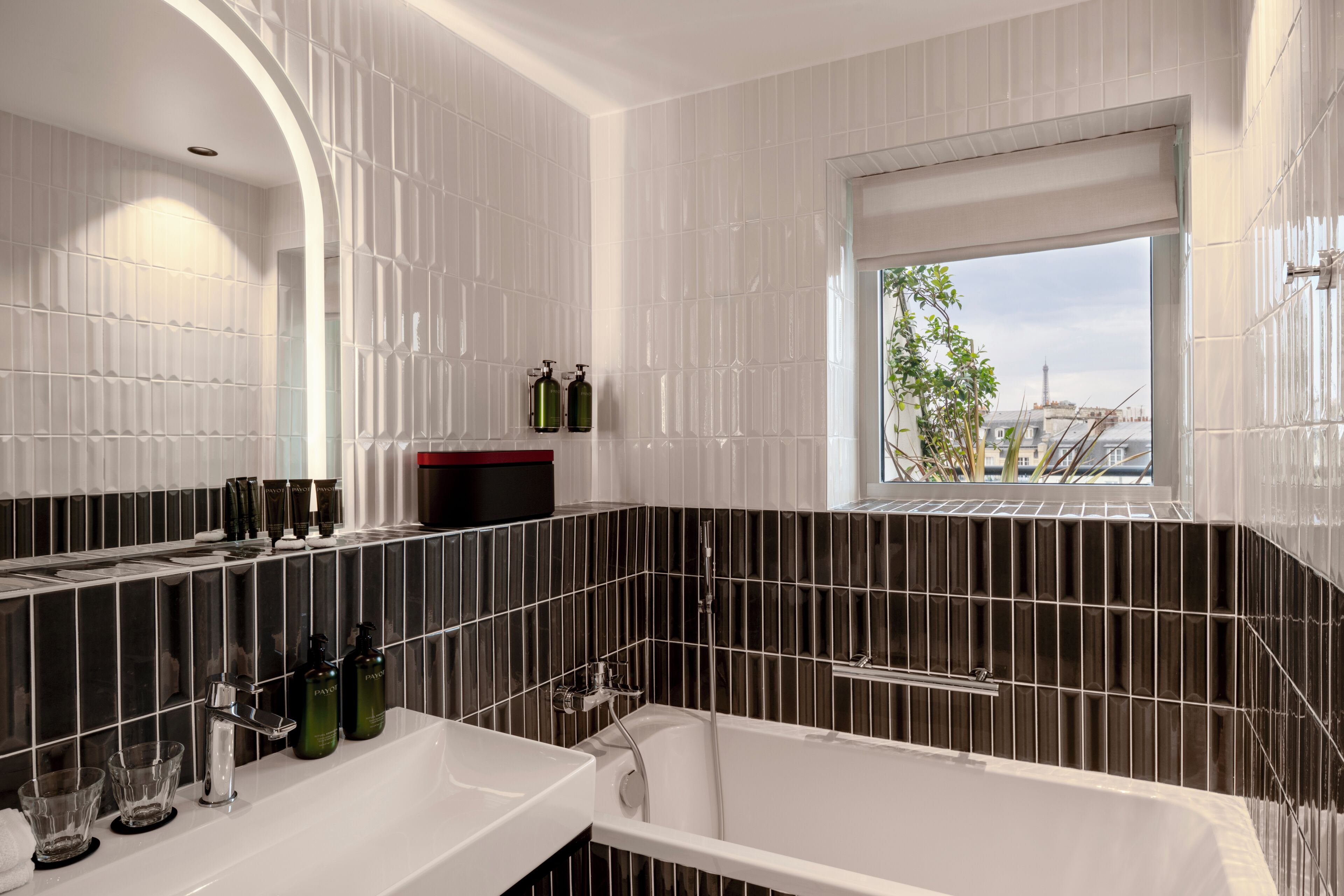 Ein modernes Badezimmer mit einer Badewanne, einem großen Spiegel und einem Fenster mit Blick auf Gebäude.