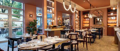 Un restaurante con varias mesas y sillas, ventanas amplias y una variedad de luminarias.