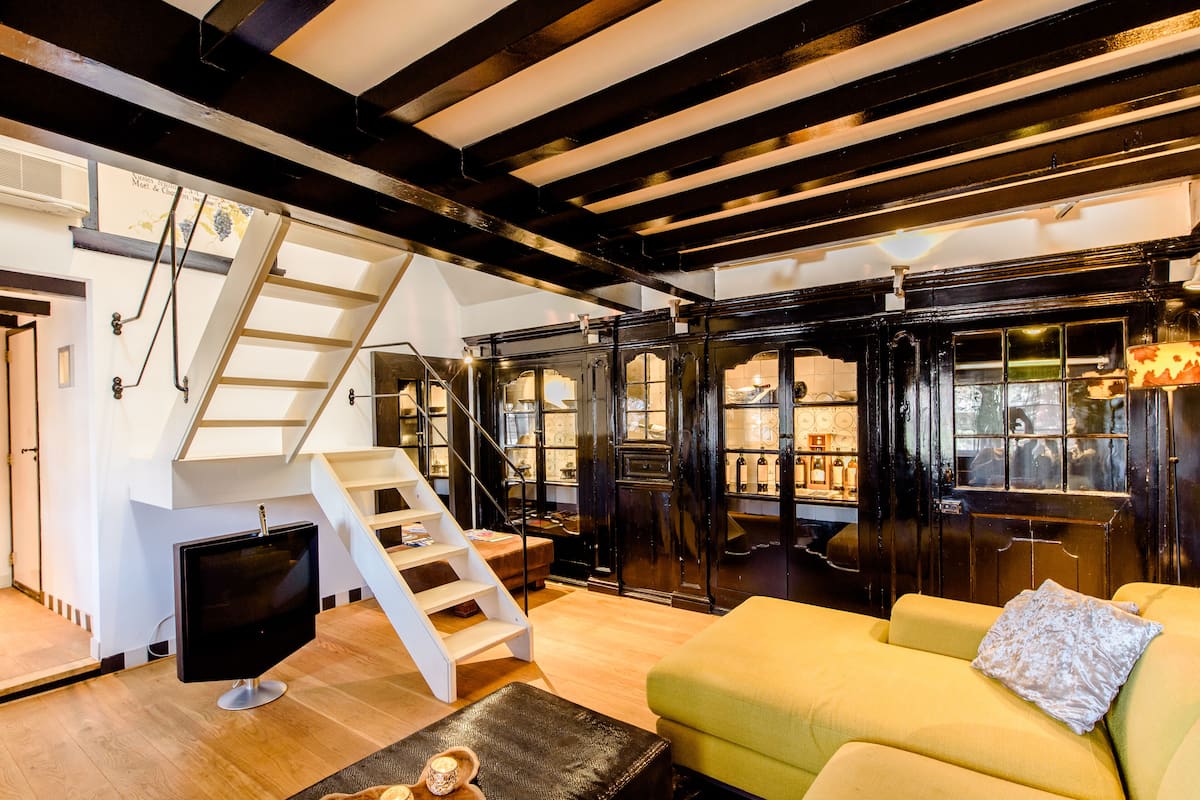 Ein modernes Wohnzimmer mit Treppe, Flachbildfernseher, gelbem Sofa und Holzboden.