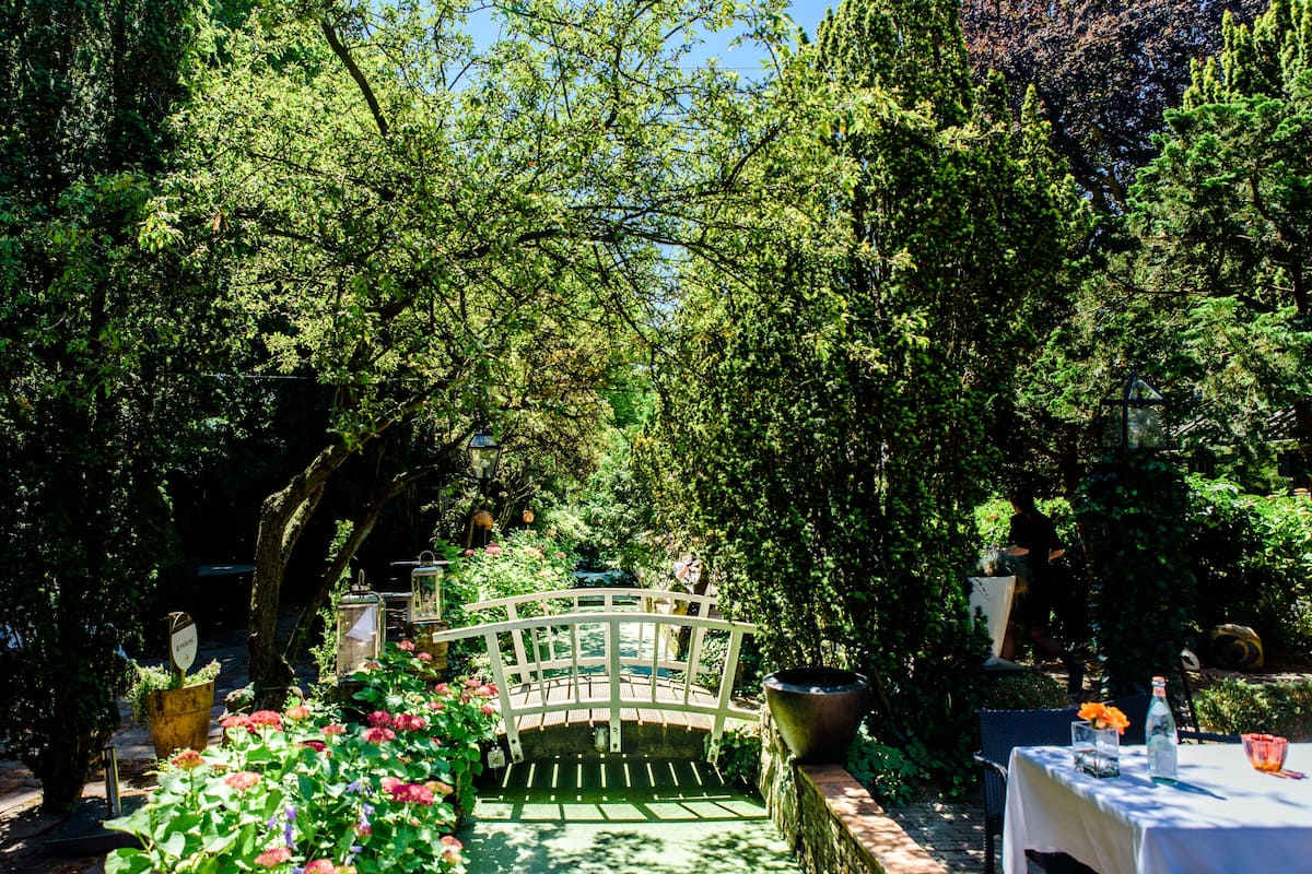Ein Garten mit einer weißen Brücke, Topfpflanzen und einem Tisch mit weißem Tuch.
