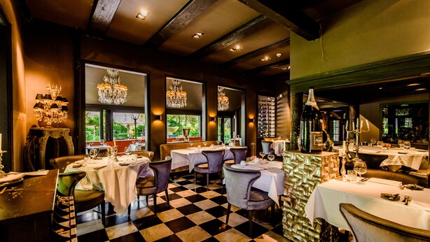 A restaurant with checkered flooring, multiple tables with white tablecloths, and chandeliers. - Luxury Vintage Hotel Villa Beukenhof (Oegstgeest)
