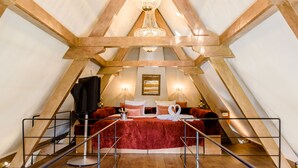 A cozy, triangular room with a vaulted ceiling, a chandelier, a bed with red bedding, and a small table with a bottle and glasses. - Luxury Vintage Hotel Villa Beukenhof (Oegstgeest)