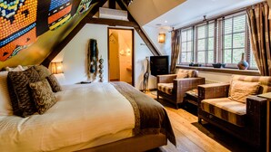 A spacious bedroom with a large bed, a sitting area with wicker furniture, and a television. - Luxury Vintage Hotel Villa Beukenhof (Oegstgeest)