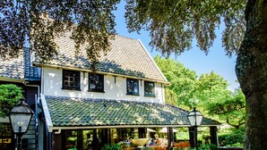 A traditional building with a tiled roof, a covered patio area, and a garden with plants and a birdbath. - Luxury Vintage Hotel Villa Beukenhof (Oegstgeest)