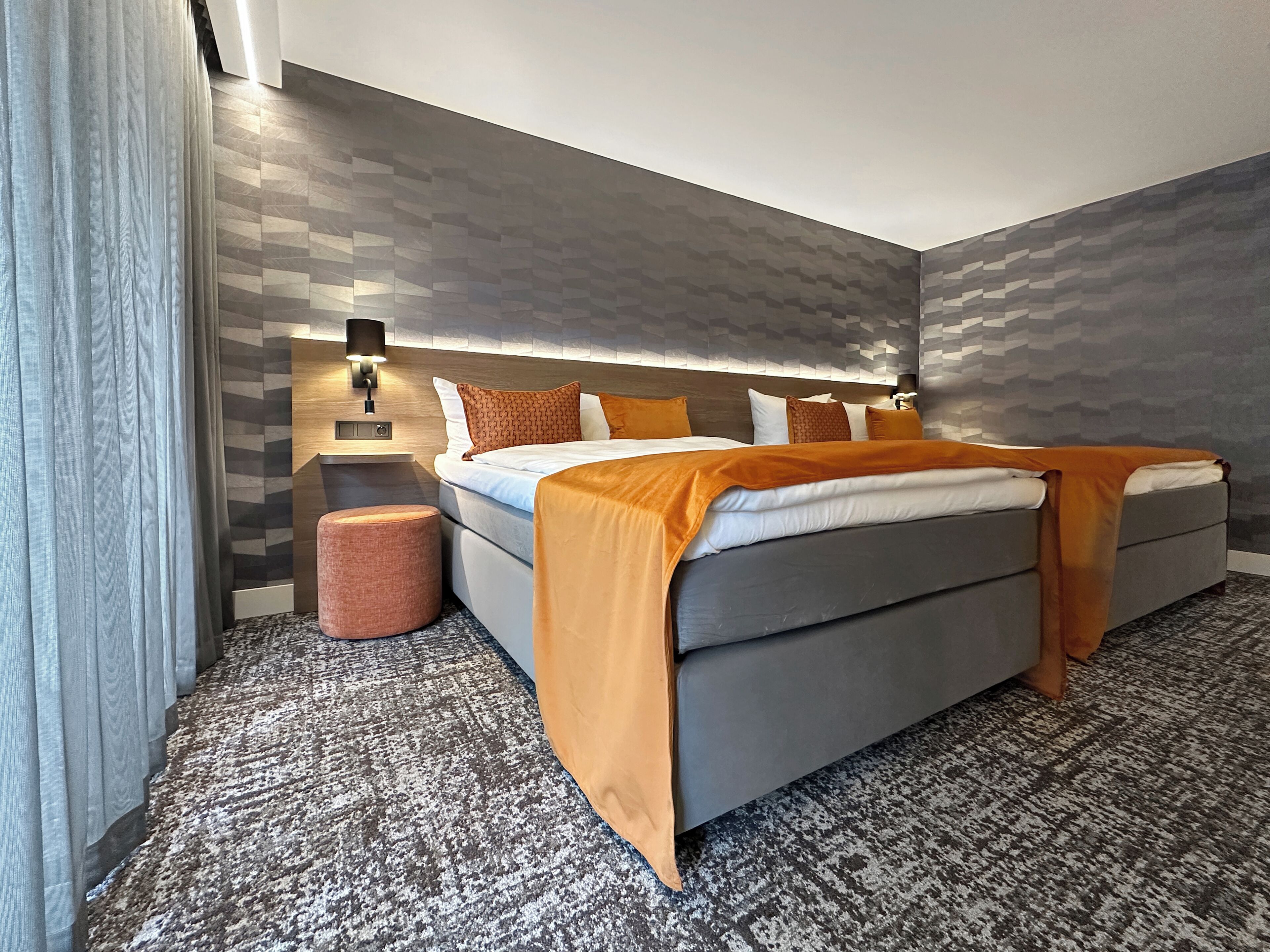 A modern bedroom with a large bed, two bedside tables, a wall-mounted light, and a textured carpet.