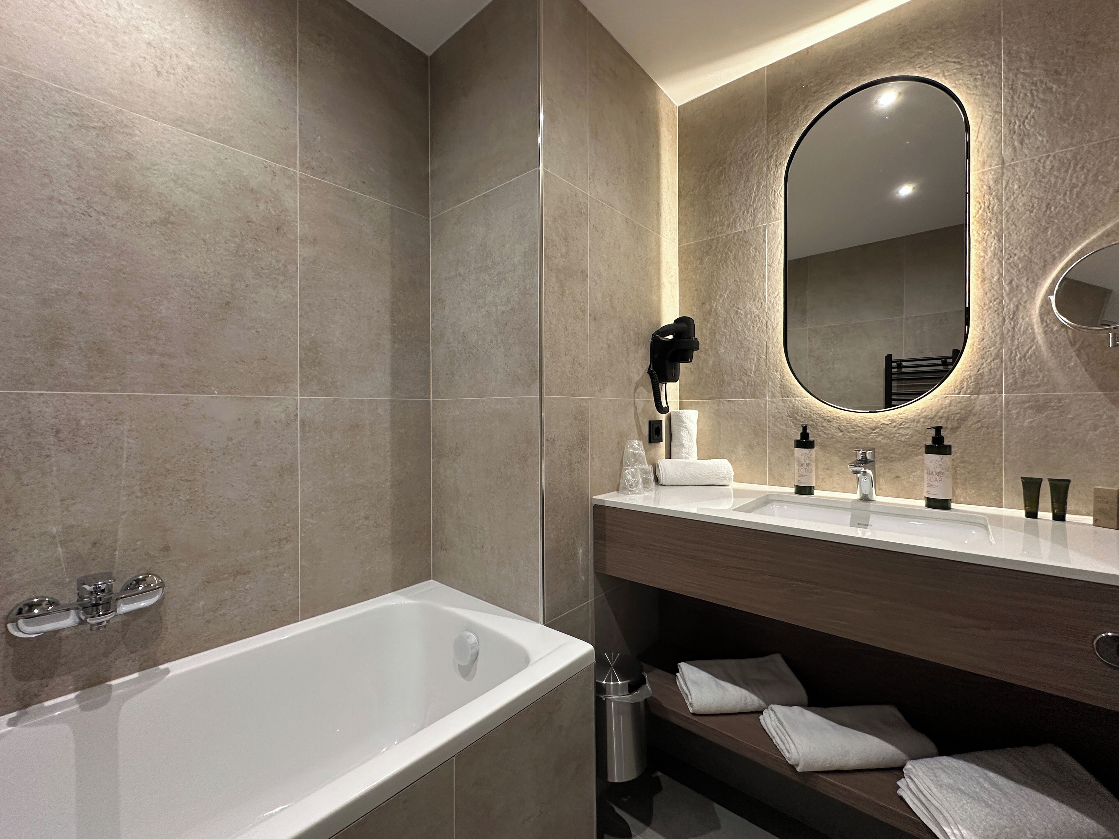 Une salle de bain moderne avec une baignoire, un meuble-lavabo avec un miroir et un sèche-cheveux fixé au mur.