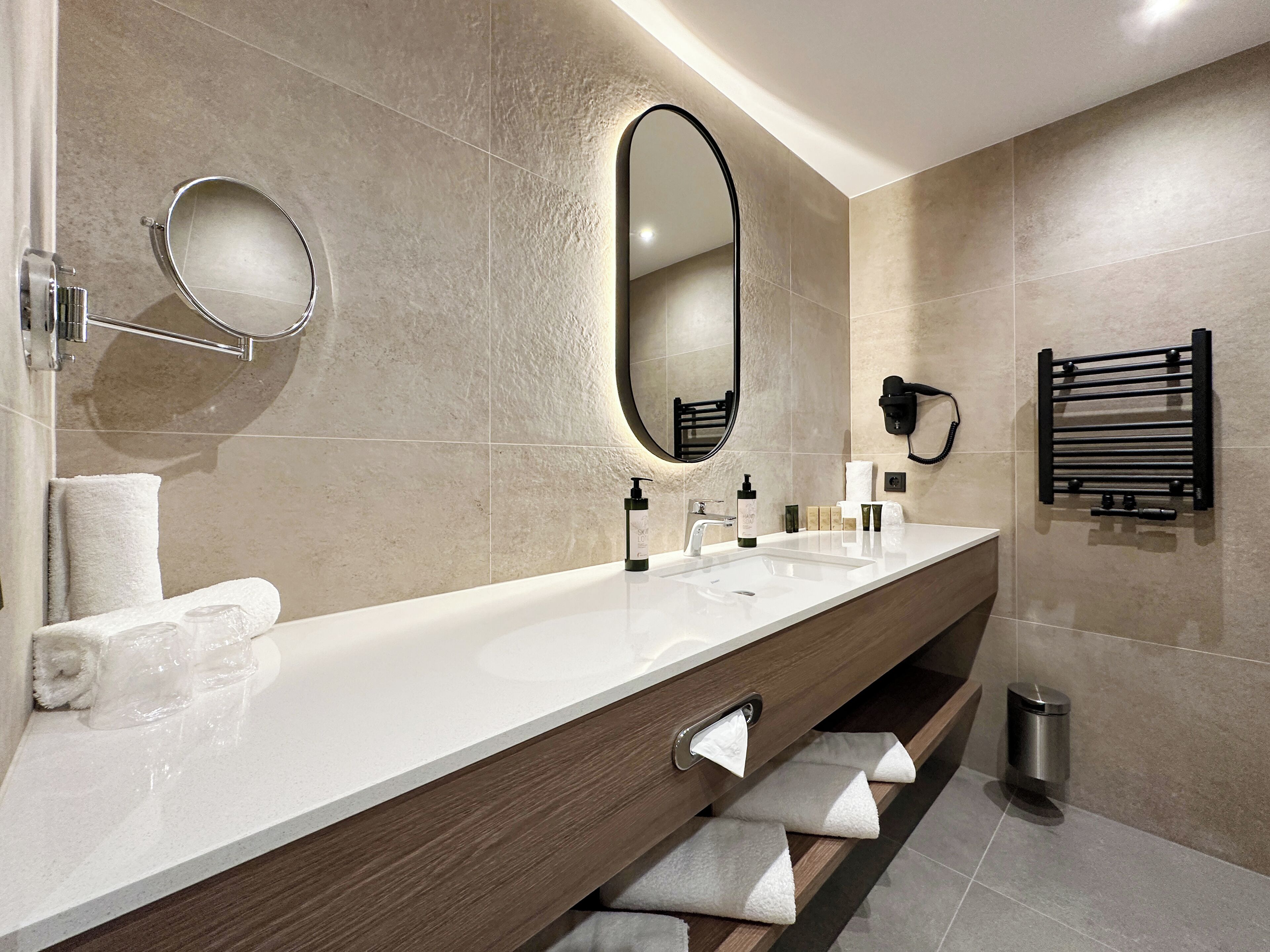A modern bathroom with a long vanity, a large mirror, a towel rack, and a hairdryer.