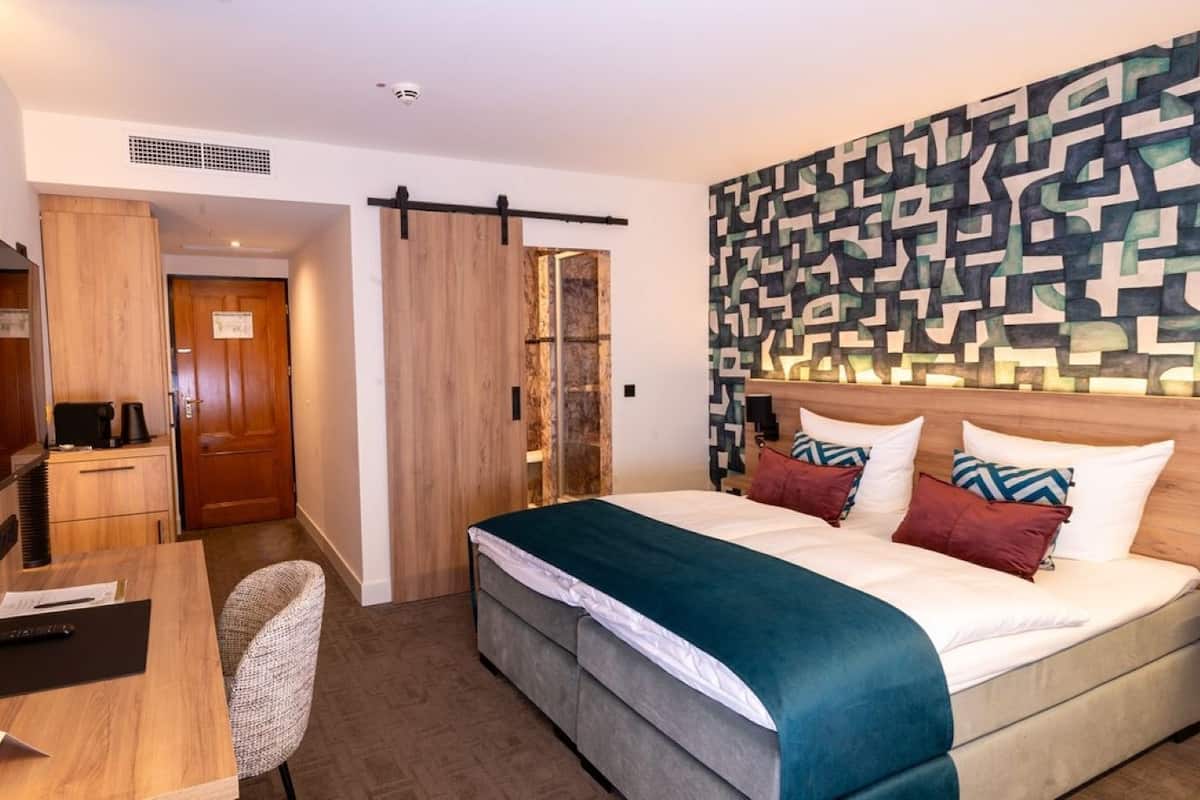 Habitación de hotel con cama, escritorio, silla, armario y una pared con diseño geométrico.