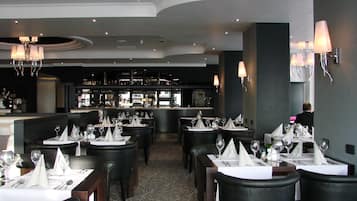 A restaurant with multiple tables set for dining, a bar area in the background, and a person seated at a table.