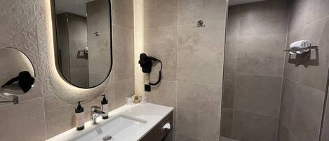 Un baño moderno con un espejo grande, lavamanos dobles, un secador de pelo y una zona de ducha.