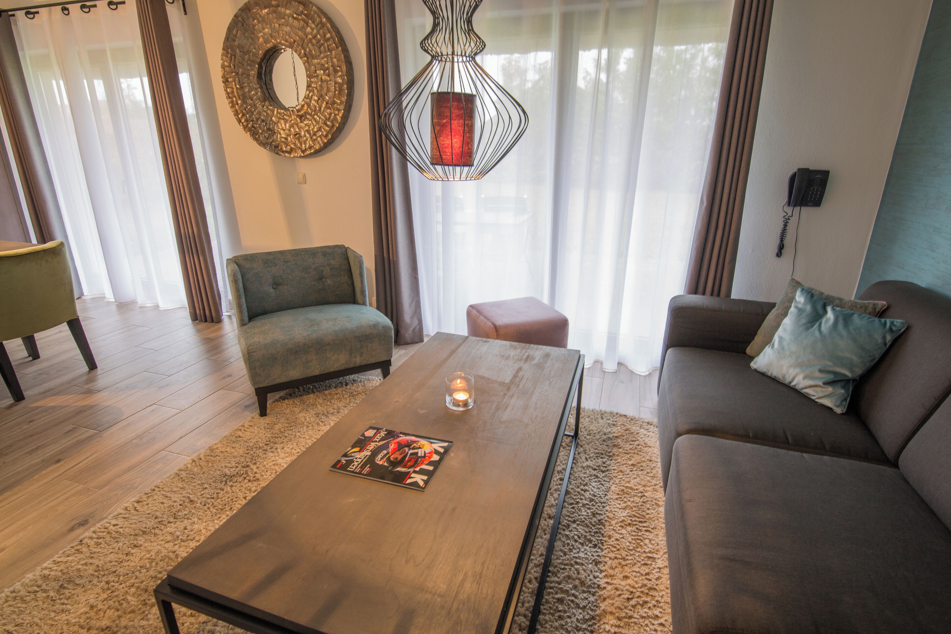 A living room with a sofa, armchair, coffee table, and a hanging light fixture.