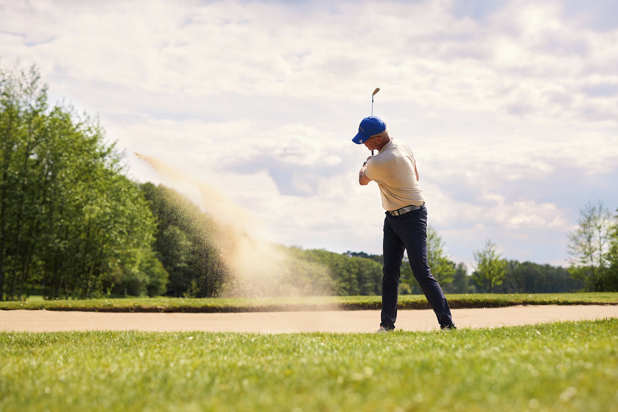 Une personne jouant au golf sur un parcours bordé d’arbres, sous un ciel dégagé.