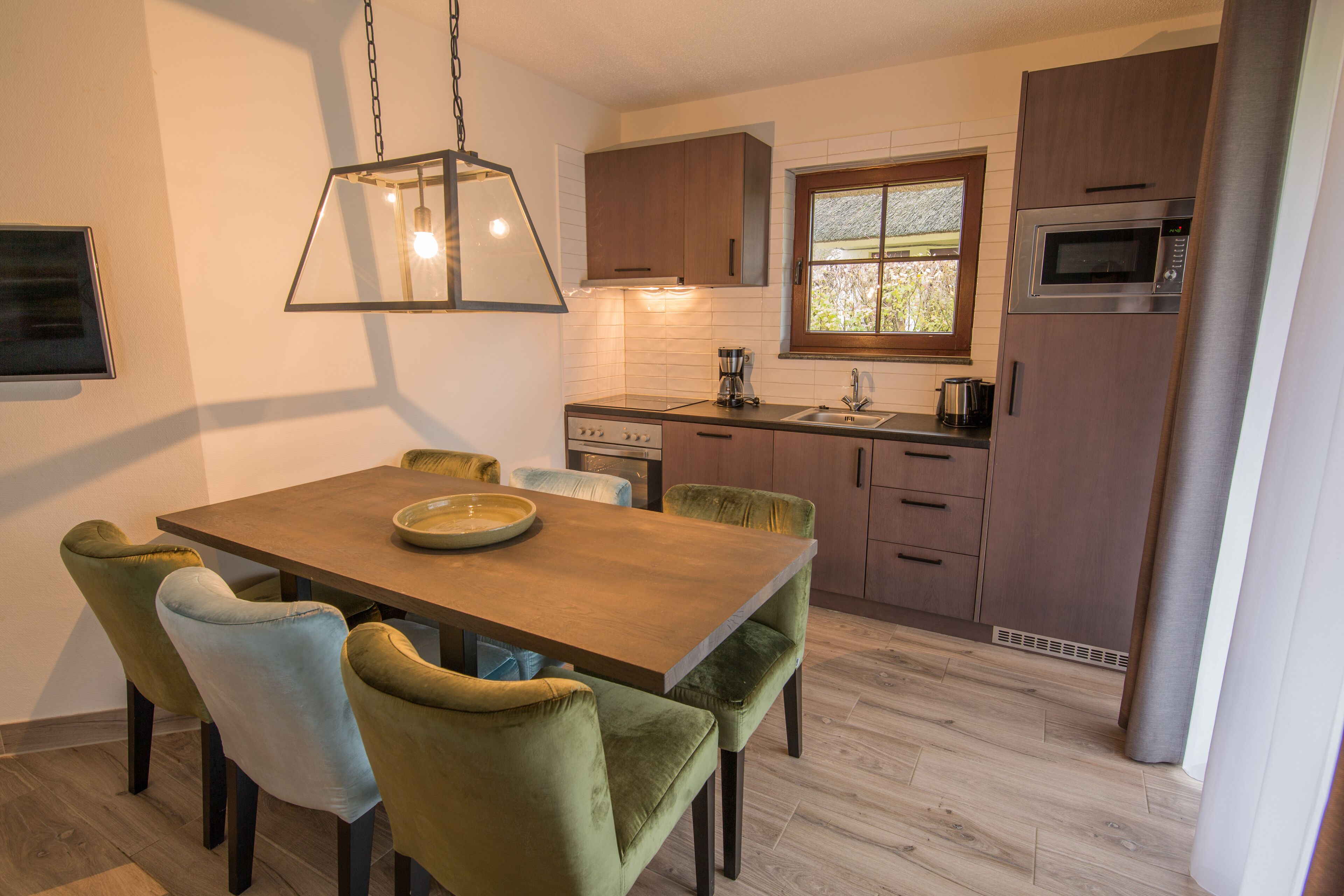 A modern kitchen with a wooden dining table, green upholstered chairs, and a stainless steel refrigerator.