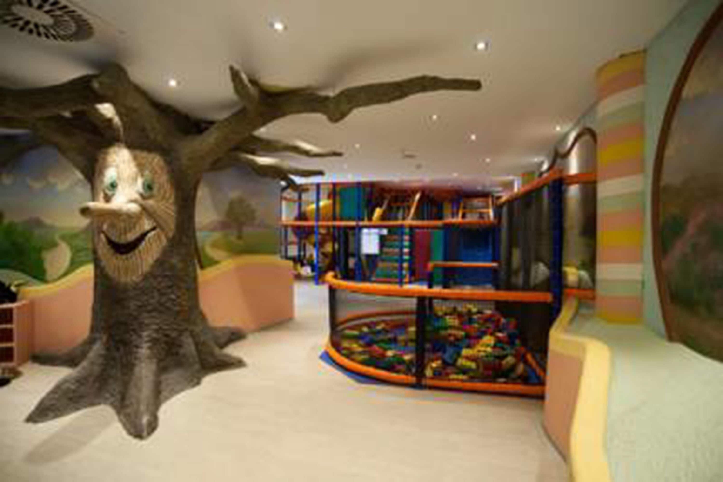 A children's play area with a large tree structure, colorful play equipment, and a ball pit.