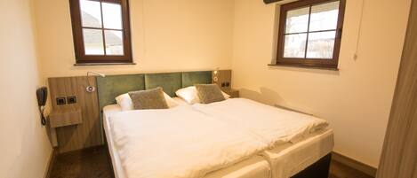 Habitación de hotel con cama doble, dos mesitas de noche, teléfono y dos ventanas con persianas.