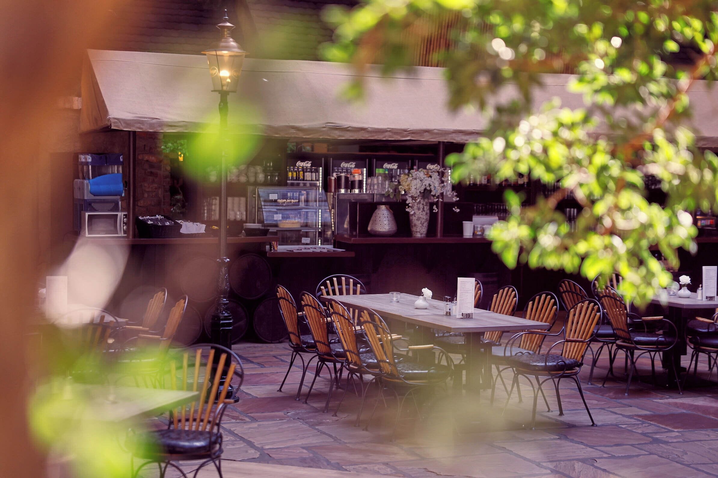 An outdoor dining area with tables and chairs, a bar with shelves of bottles, and a street lamp.
