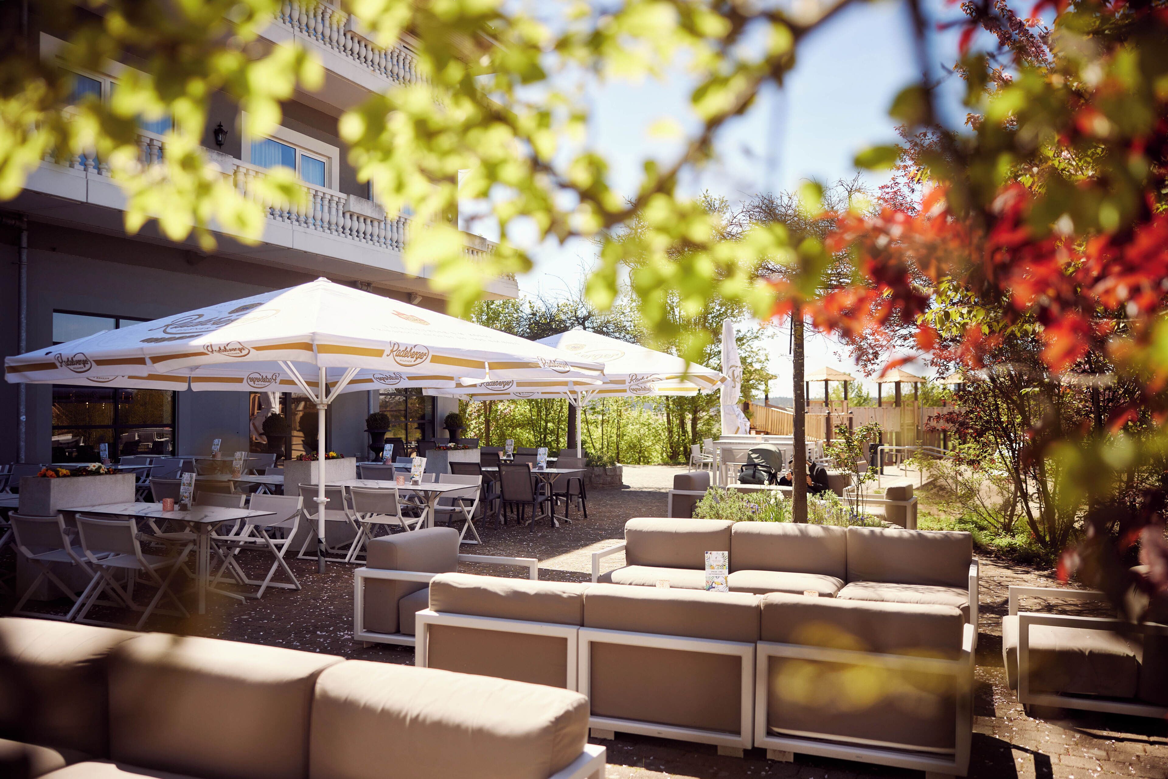 An outdoor seating area with multiple tables and chairs, a covered dining area, and a building with balconies.
