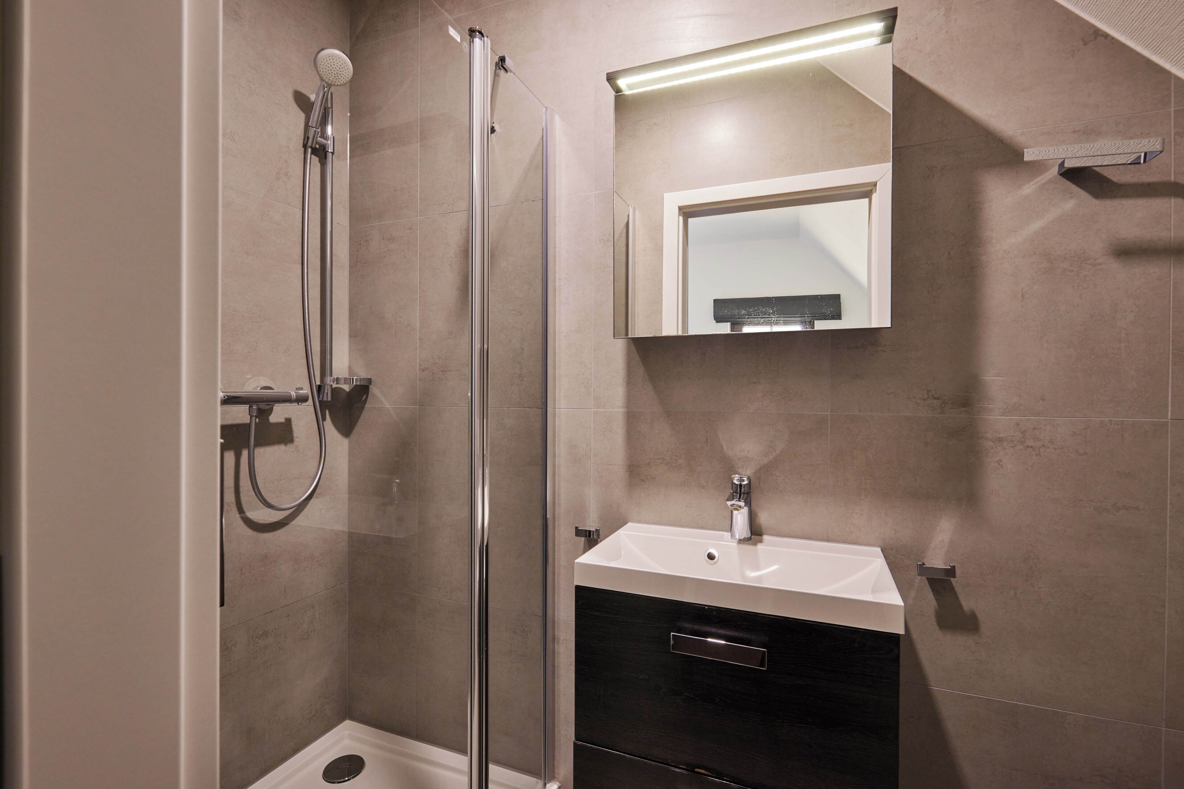 Un baño moderno con cabina de ducha de vidrio, un lavabo blanco y un espejo sobre el mueble.