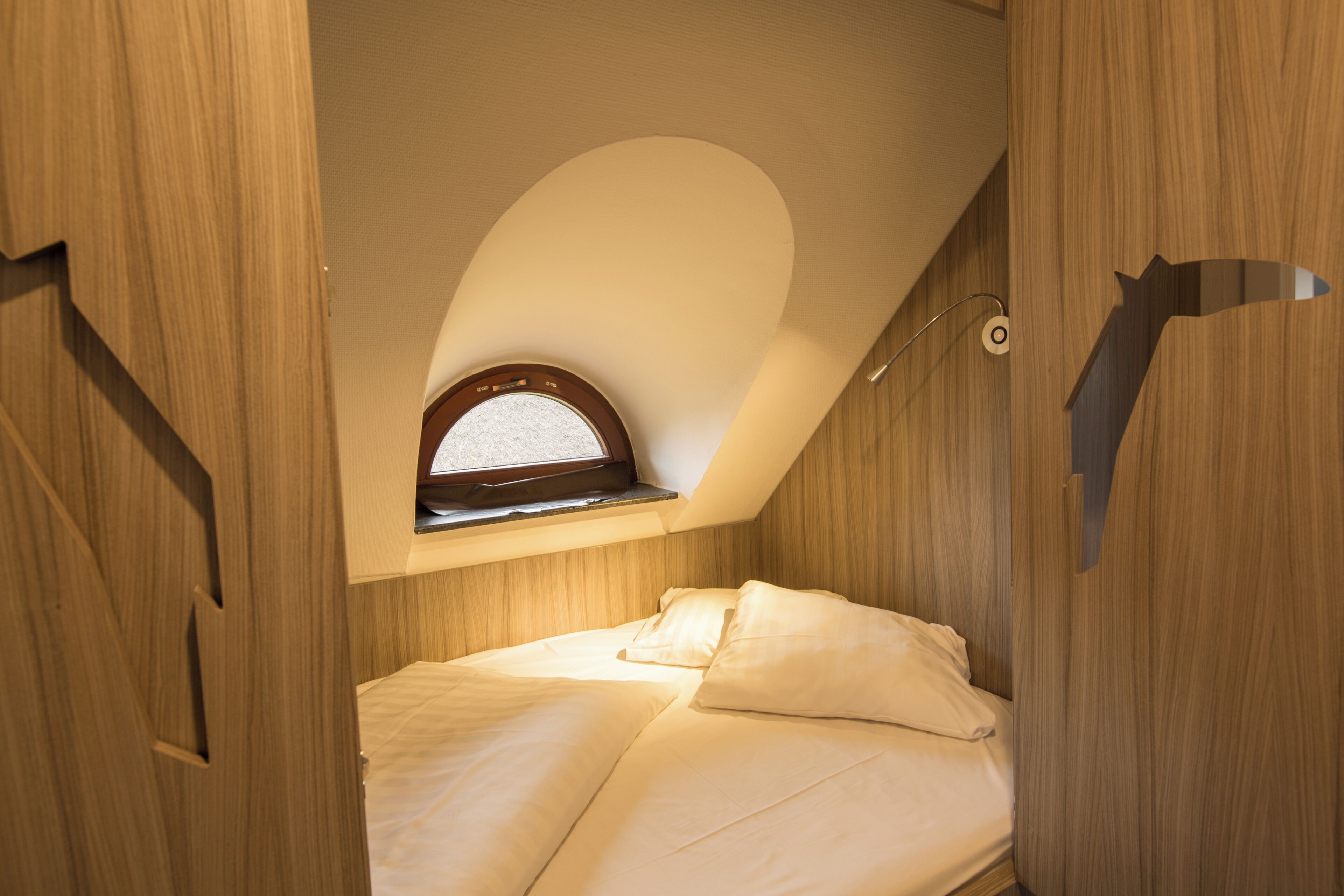 Un dormitorio con techo inclinado, tragaluz y cama con ropa blanca.