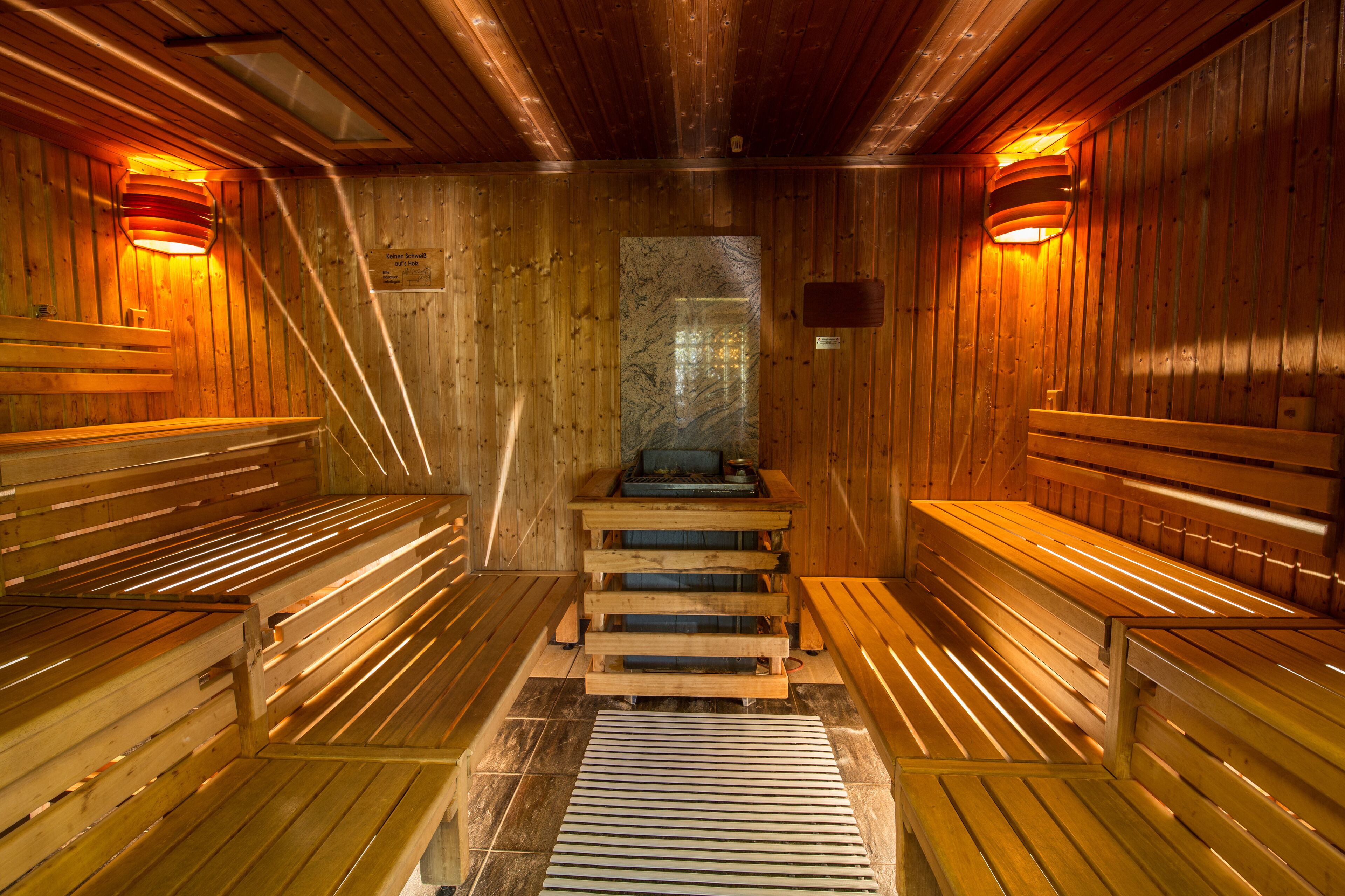 A sauna with wooden benches and benches, a central stone feature, and wooden walls.