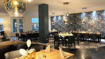 A restaurant with multiple dining tables, black chairs, and hanging spherical light fixtures.
