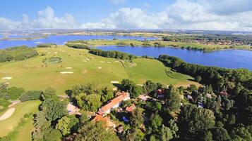 An aerial view of a golf course with a clubhouse, surrounded by water bodies and greenery.