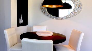 A dining area with a round table, white chairs, a black pendant light, and a decorative mirror with a pearl-like frame.