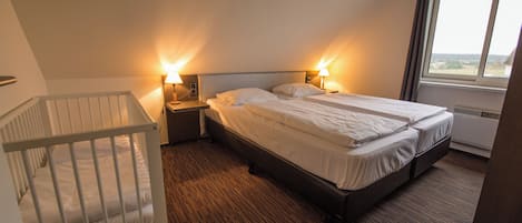 A hotel room with a crib, a double bed, two bedside lamps, and a window with a view.