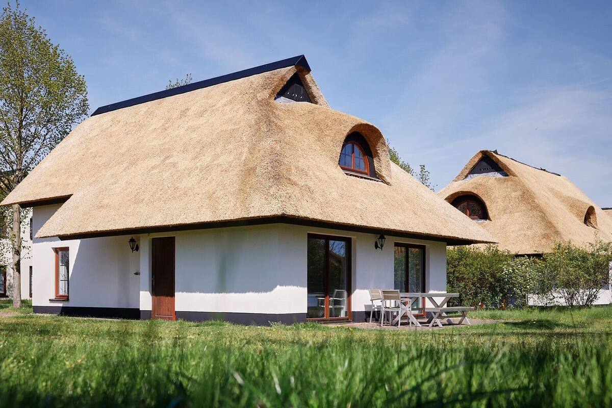 A thatched-roof house with a white exterior, a door, and a small patio area with chairs.