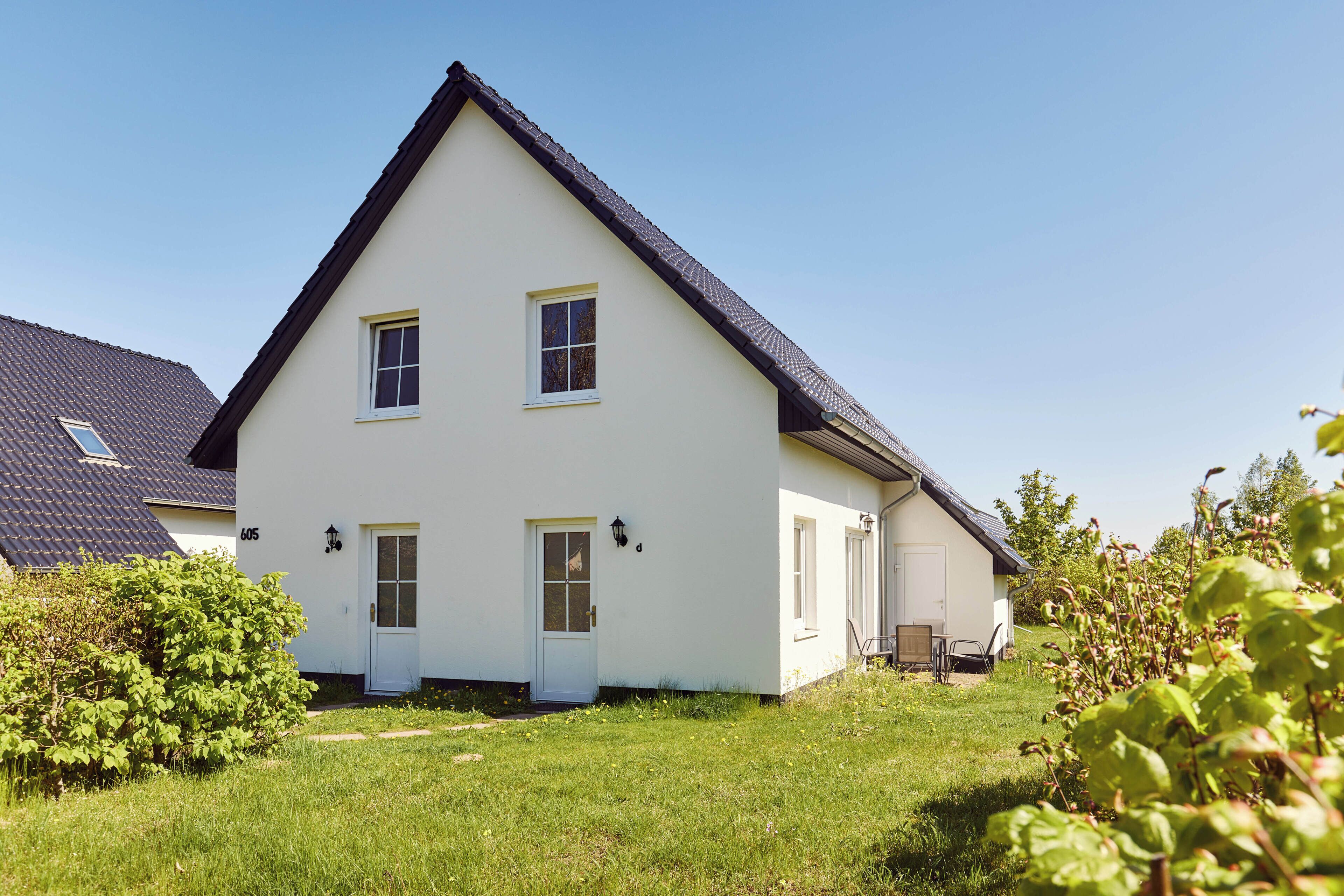 Ein zweistöckiges Haus mit weißer Fassade, dunklem Dach und kleinem Vorgarten.