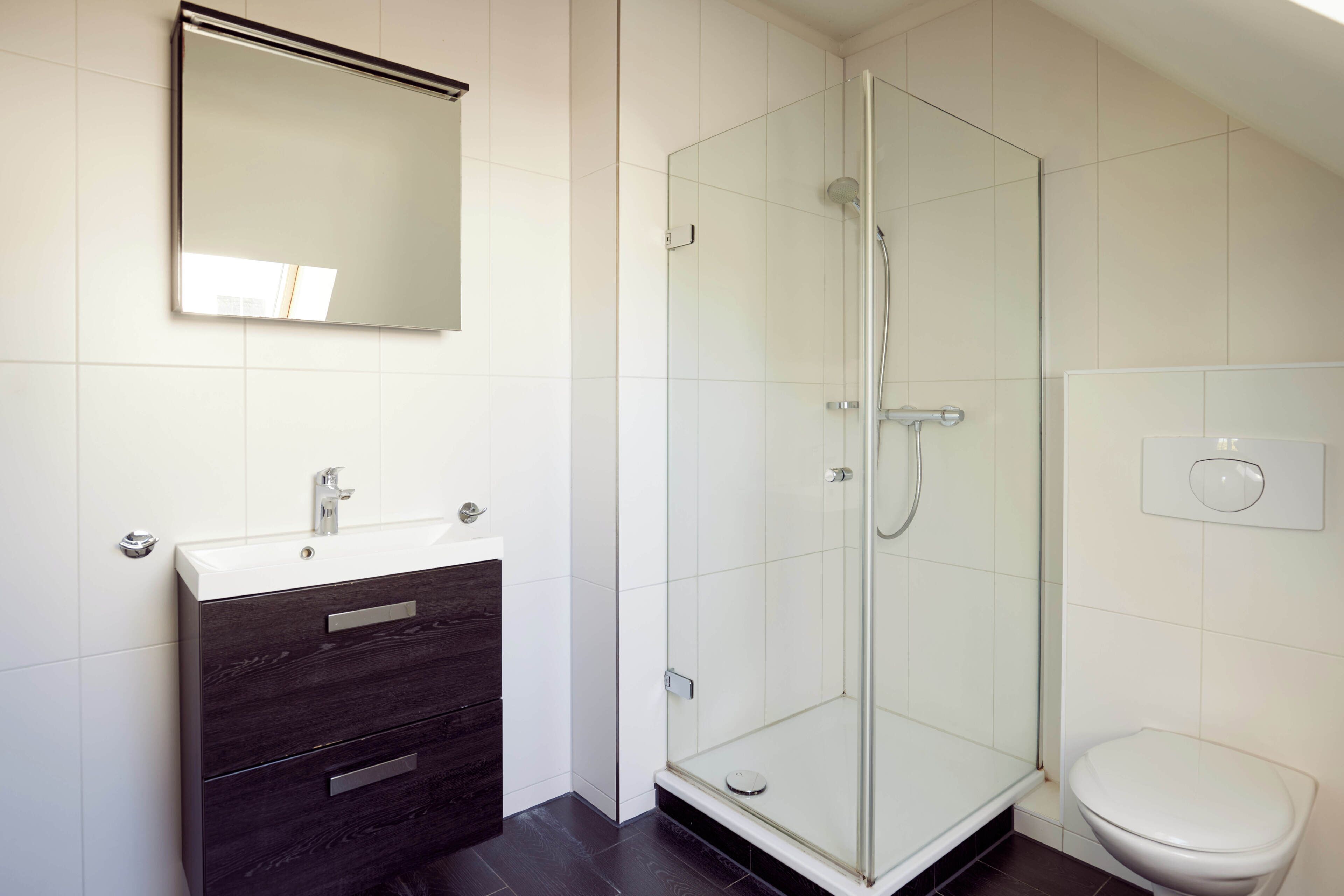 A bathroom with a glass shower enclosure, a white sink, and a dark wooden vanity.